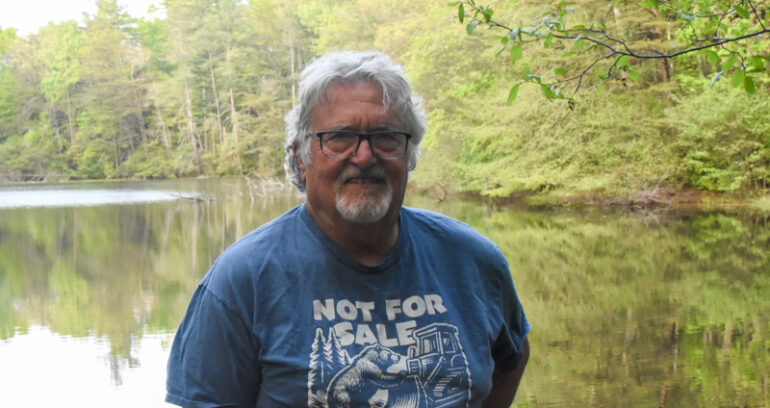 Roger standing in front of the lake wearing a tshirt that says, "Not for sale".